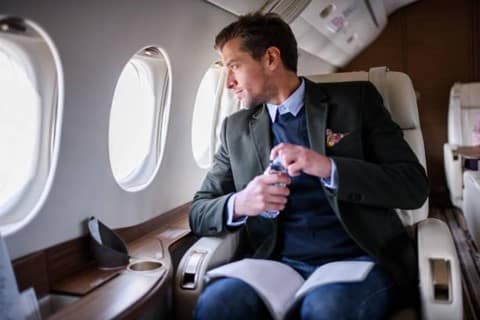An elegant man is sitting inside the airplane, holding distilled bottled water.
