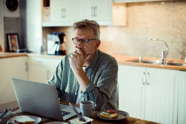 A mature man using a laptop is thinking about whether investing in CPAP pillows is worth it.