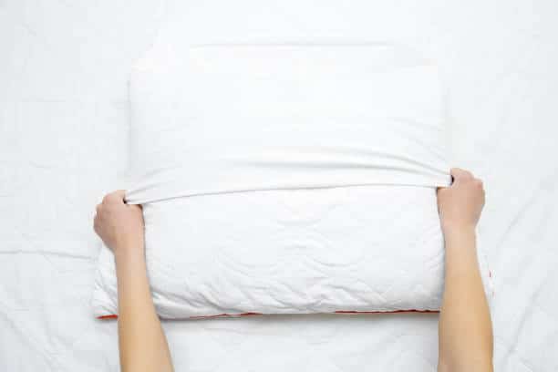 Woman's hands on mattress surface changing white cotton cover on pillow.