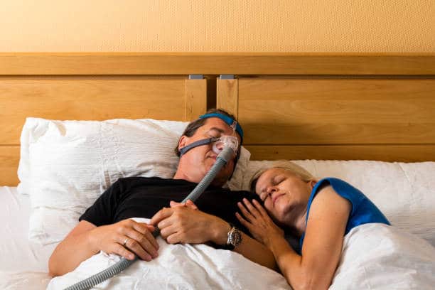 A couple resting soundly with the aid of a CPAP machine.