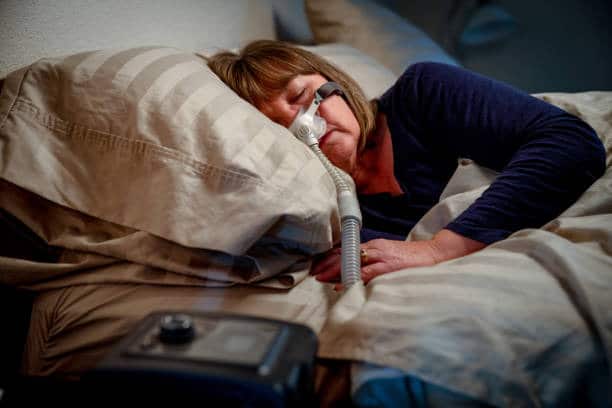 A photo of a woman sleeping in her bed while utilizing CPAP machine